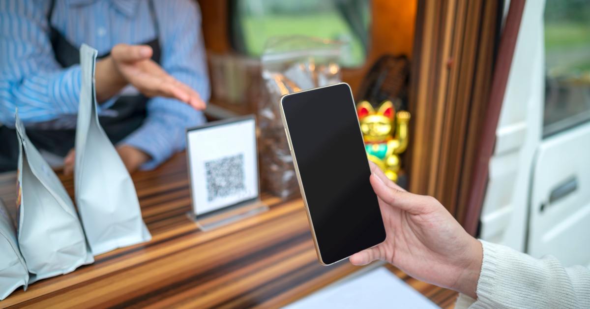 A person stands at the checkout counter of a coffee shop truck with their phone out to scan the QR code.