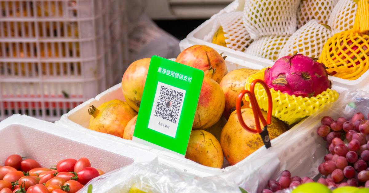 A market with a table full of white baskets containing fresh produce. There is a QR code in one of the baskets.