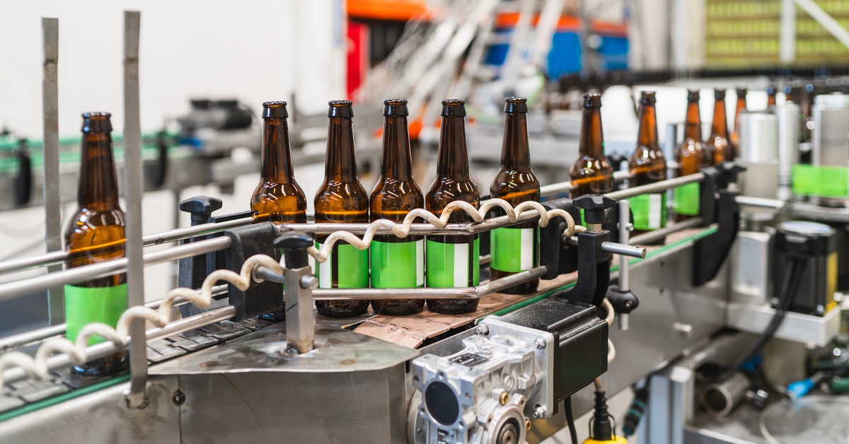 A conveyor belt in a warehouse with amber glass bottles rolling through after they receive a green label.