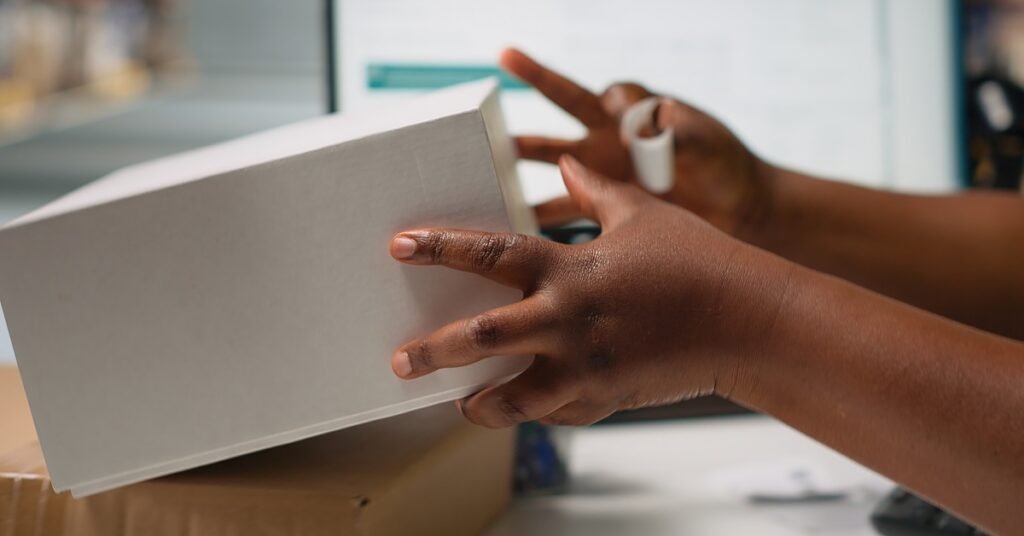 A Black employee at the desk places a label on a white box. The label is small and sticks to the box.