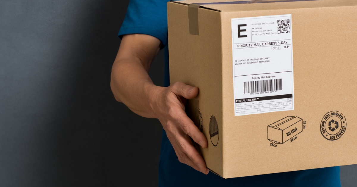 A person holds a medium-sized box ready for shipping. The box has a white label on the outside corner.